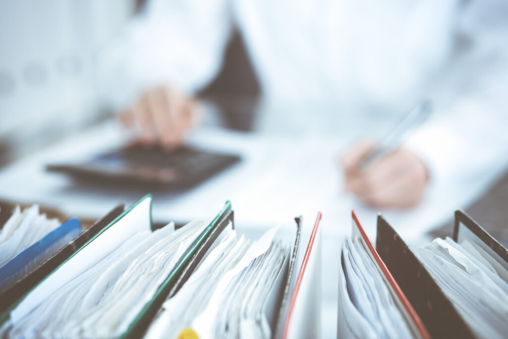 Binders of papers waiting to process by bookkeeper woman or financial inspector, close-up. Business portrait. Audit or tax concepts.
