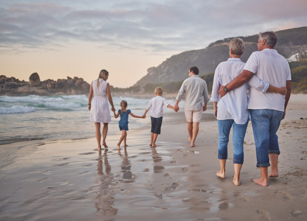 Family, generations and back with walking, beach and sunset with men, women and children with love. Parents, grandparents and kids by ocean, holding hands and bond on summer vacation with solidarity.